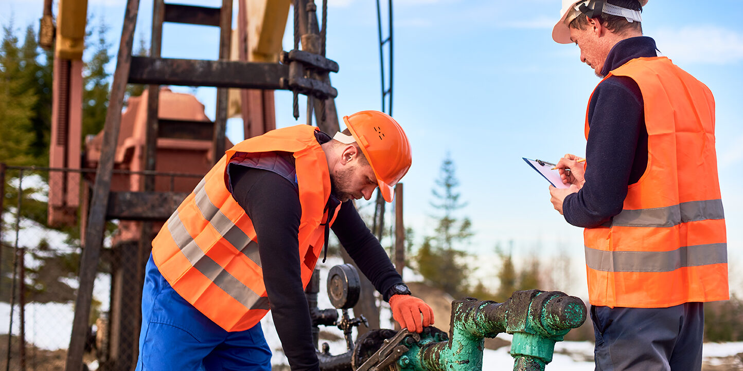 Oil workers in uniforms controlling progress work at local oil pump station on sunny day oilfield services staffing