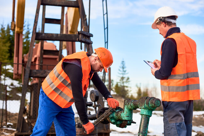 Oil workers in uniforms controlling progress work at local oil pump station on sunny day oilfield services staffing
